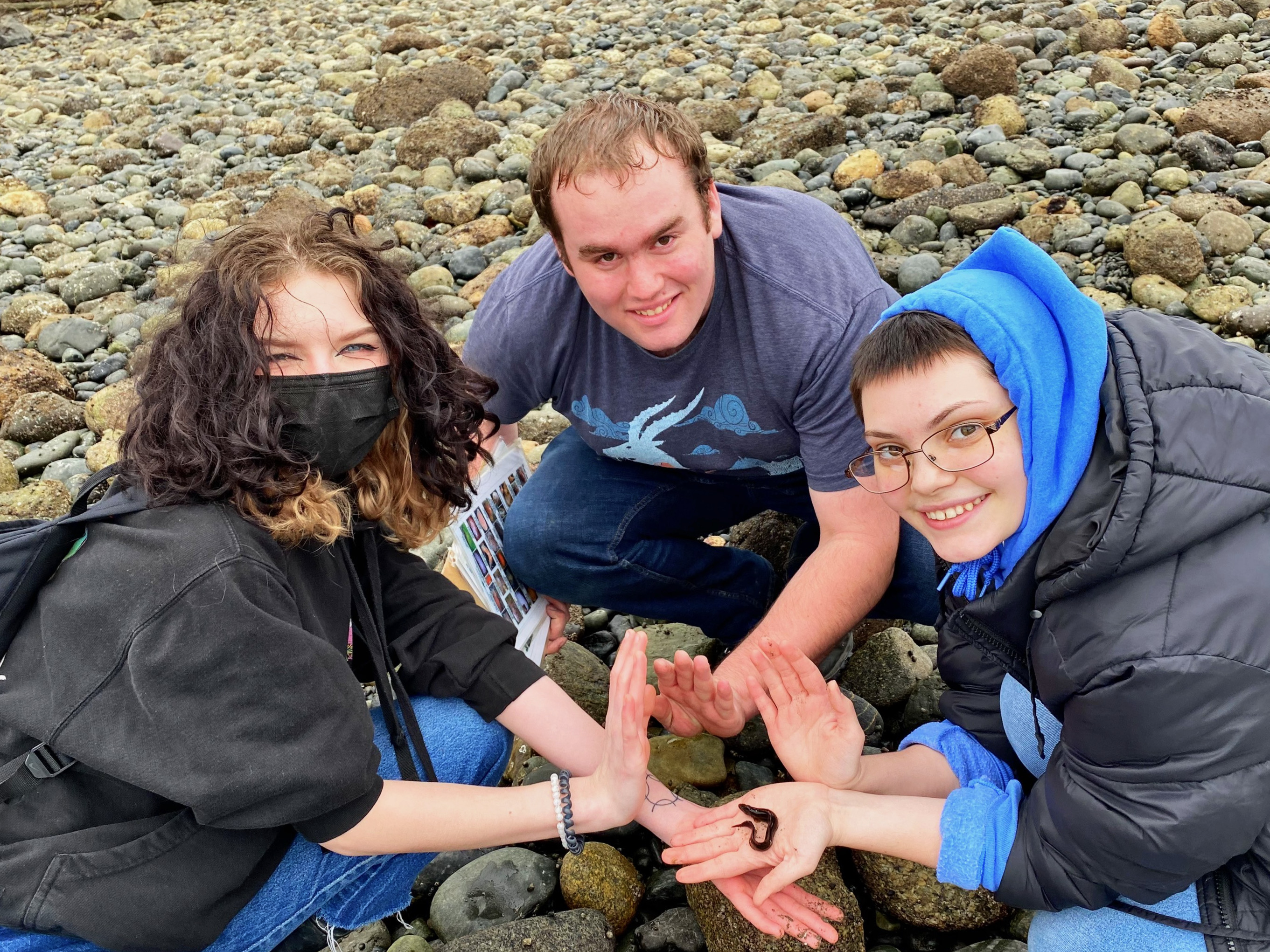three students on beach holding worm