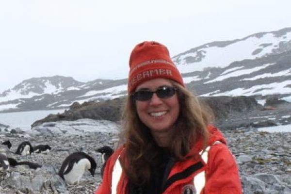 Suzanne wears a cold weather jacket and smiles, with penguins in the background